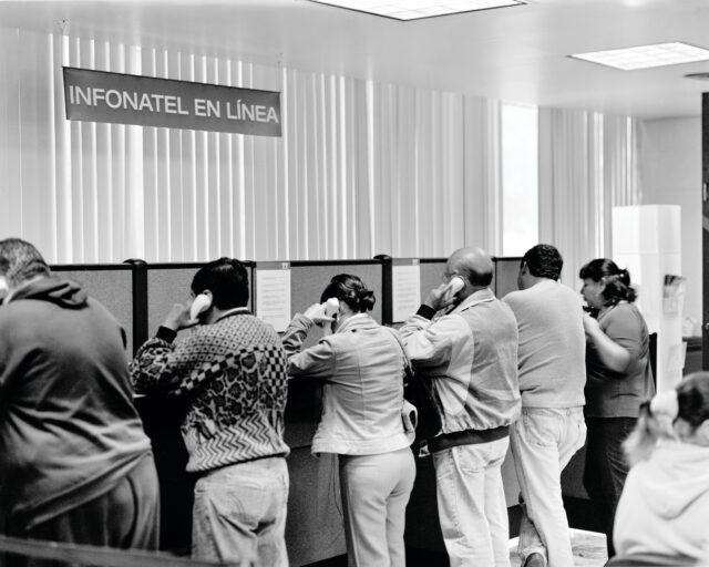 A black and white photo of half a dozen or so individuals facing away from the camera holding phones to their ears.