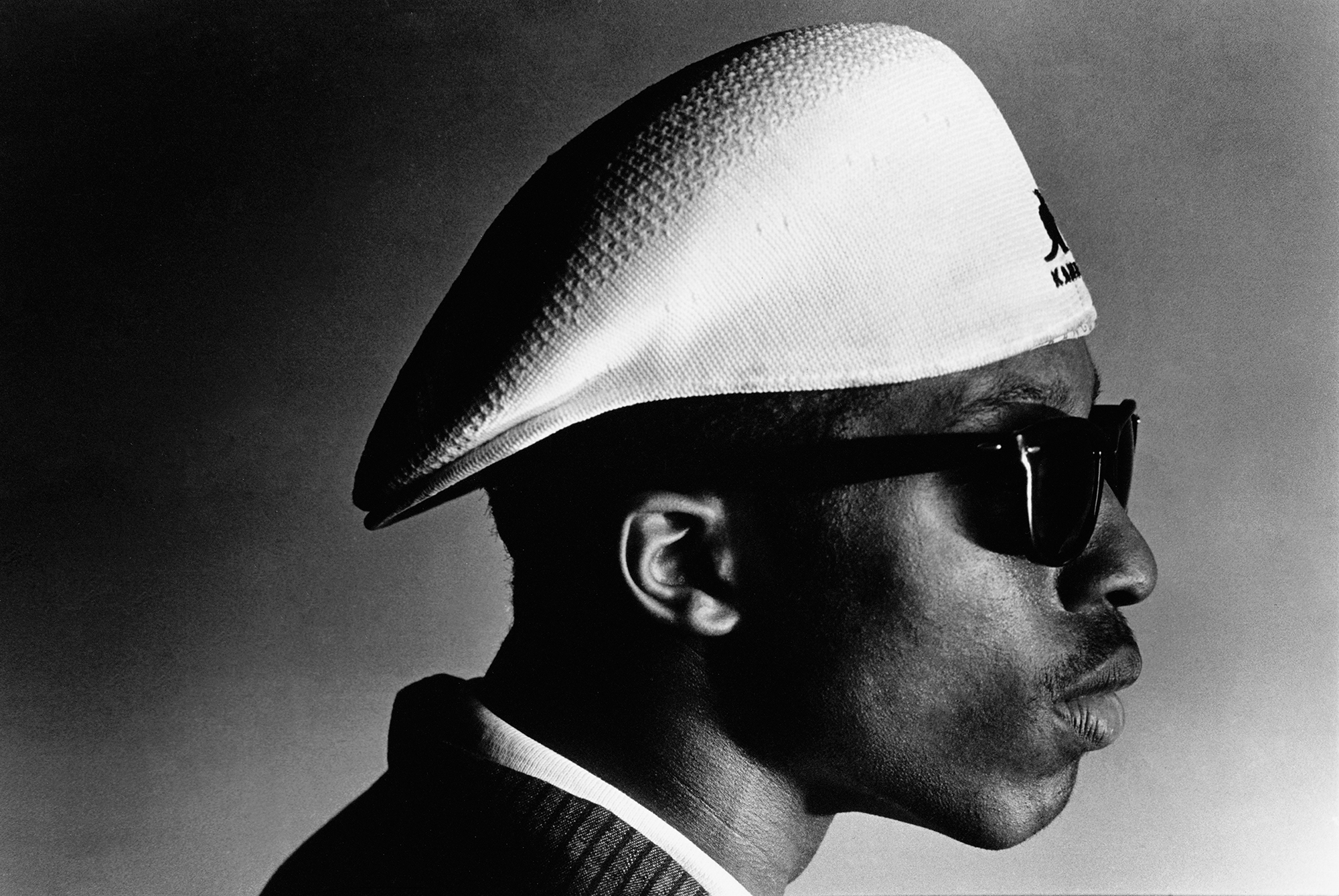 A black and white portrait of a young black man in a white hat and sunglasses.